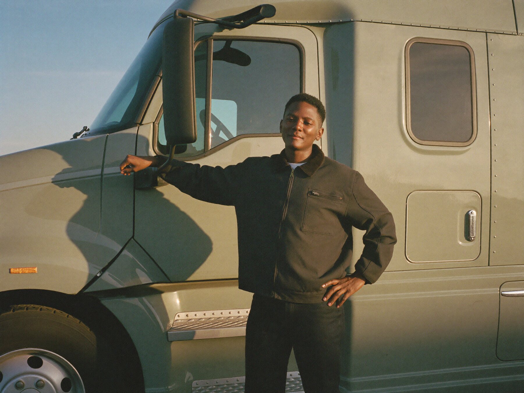 An owner-operator standing beside his semi truck at golden hour.