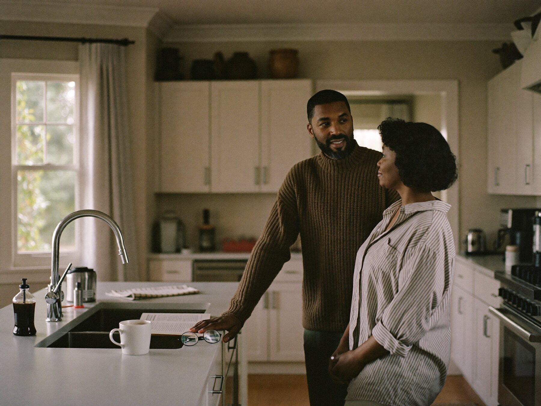 A couple in their fifties talking over coffee in their kitchen.