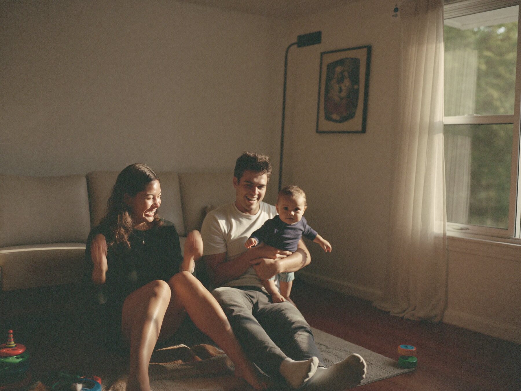 New parents laughing on the living room floor with their baby.