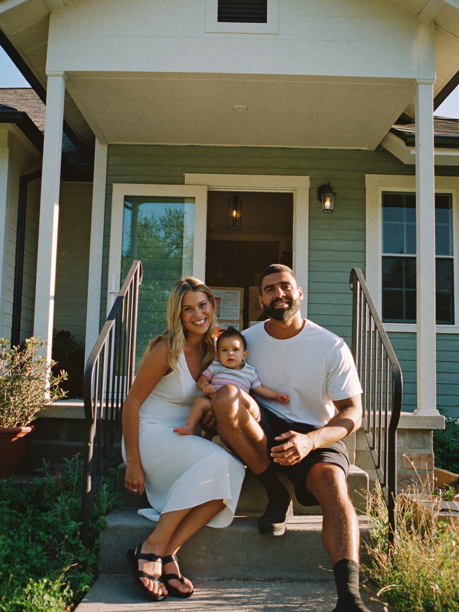 Young parents with their baby on the front steps of their first house.